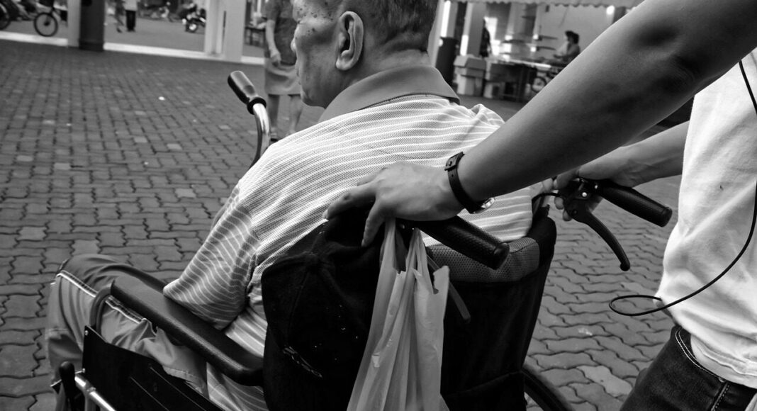 A person pushing an elderly man in a wheelchair.