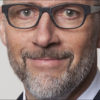 A man with glasses, a greying beard, and a suit looks into the camera with a slight smile, embodying the approachable yet professional demeanor often found in Human Resources.