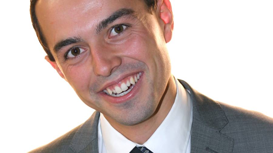 A man in a grey suit and white shirt with a tie smiles at the camera against a plain white background, showcasing his expertise in Human Resources.