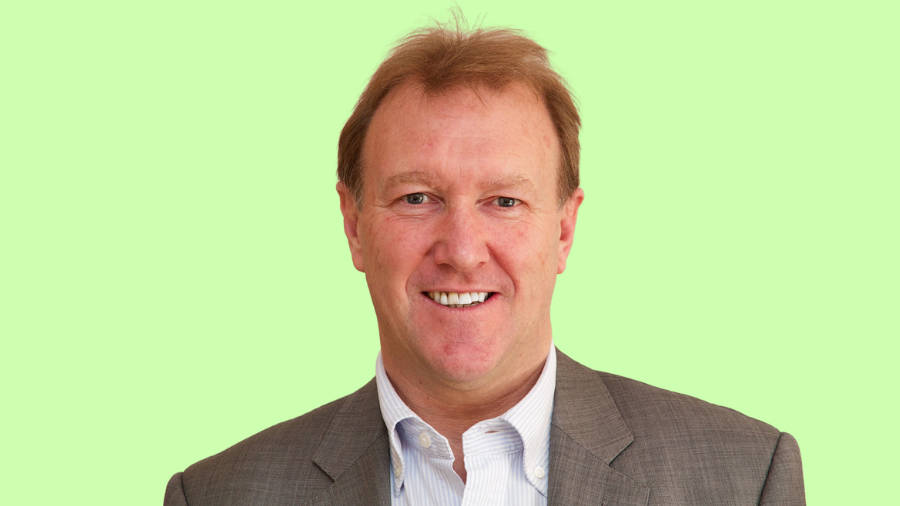 A middle-aged man with short brown hair, identified as Andrew Mawson, smiles at the camera. He is wearing a grey suit jacket over a white shirt. The background is a light green color.
