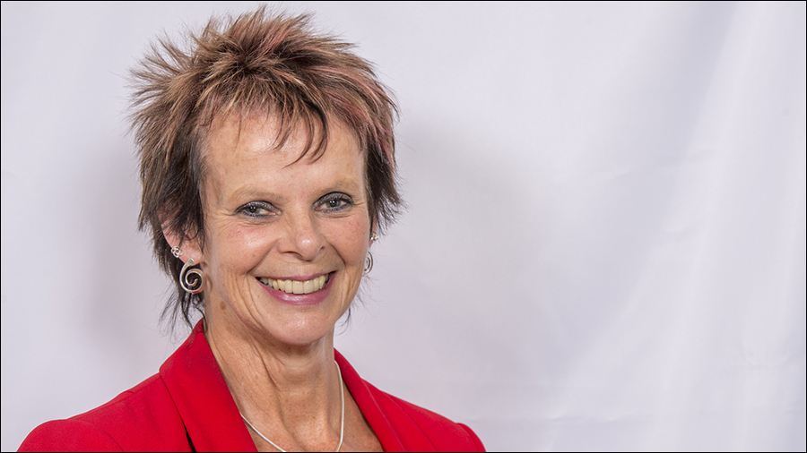 A woman with short, spiked hair and silver earrings is smiling in front of a white background while wearing a red blazer, embodying the essence of HR and people management.