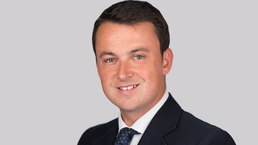 A man wearing a dark suit, white shirt, and polka dot tie is smiling against a plain background, exuding confidence and professionalism—qualities essential in Human Resources.