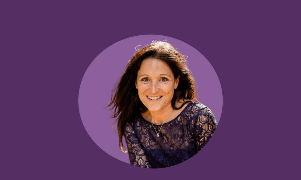 A smiling woman with long brown hair, wearing a lace top and a necklace, is centered in a circular frame on a purple background, embodying the essence of fertility at work.