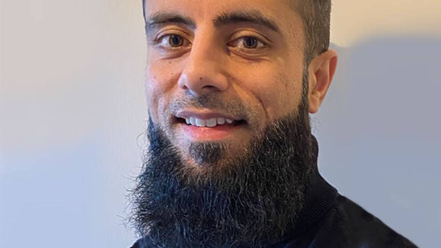 A man with a beard and mustache is smiling at the camera. He is wearing a dark-colored shirt with a light background behind him, embodying the approachable and professional demeanor often seen in Human Resources professionals.