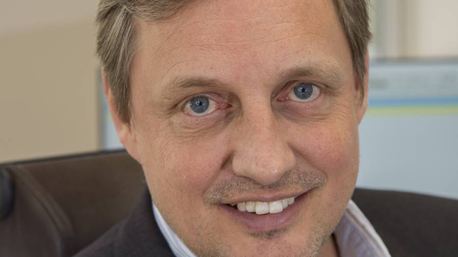 A man with short light brown hair and blue eyes is smiling at the camera. He is wearing a dark suit jacket and a light-colored shirt, embodying professionalism in Human Resources. The background is slightly blurred.