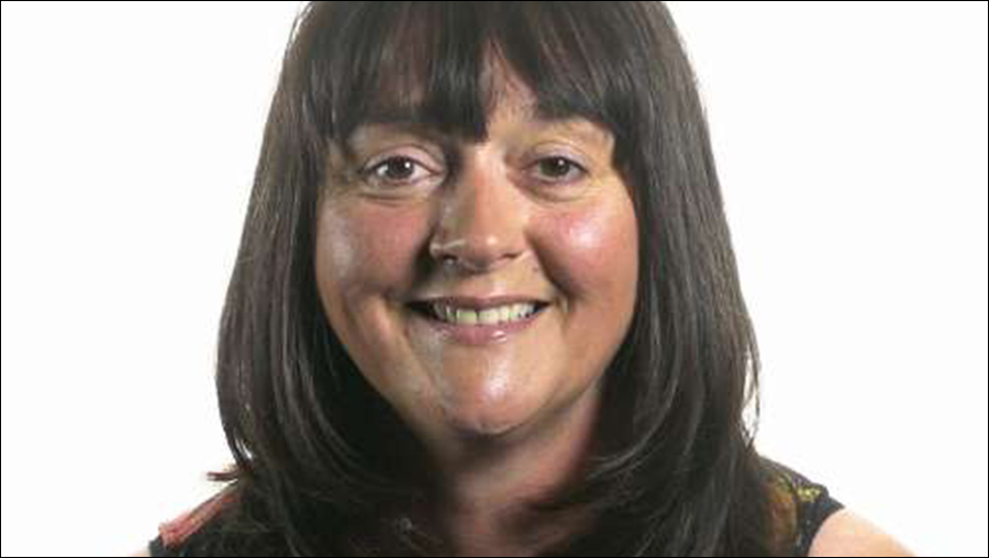 A woman with straight, dark hair and bangs smiles at the camera against a plain white background, exemplifying the professional warmth often found in Human Resources.