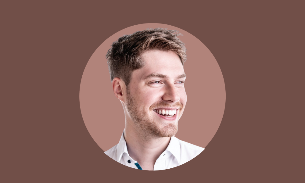 A man with short hair and a beard, dressed in a white shirt, is smiling and looking to the right. The brown background adds warmth, hinting at a welcoming atmosphere akin to intuitive HR Software.