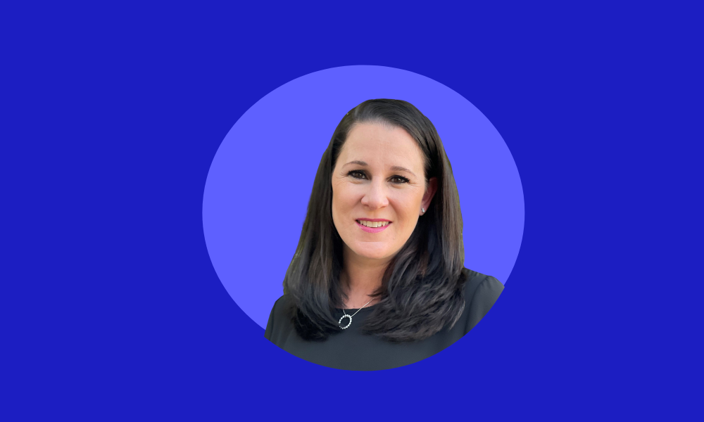 A woman with long dark hair, wearing a navy top, is smiling in front of a blue background, perhaps celebrating her newfound freedom in the wake of The Great Resignation.