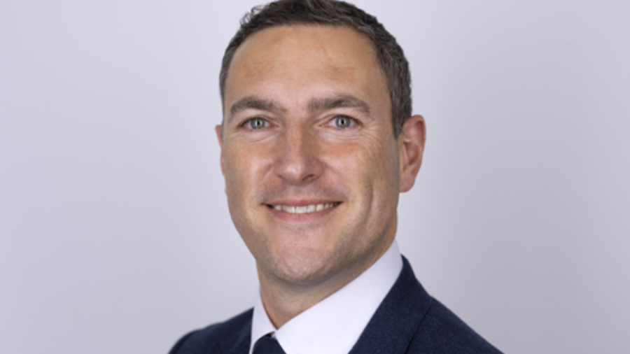 A man in a suit and tie with short dark hair and a slight smile, standing against a plain light background, exuding confidence in Personnel management.