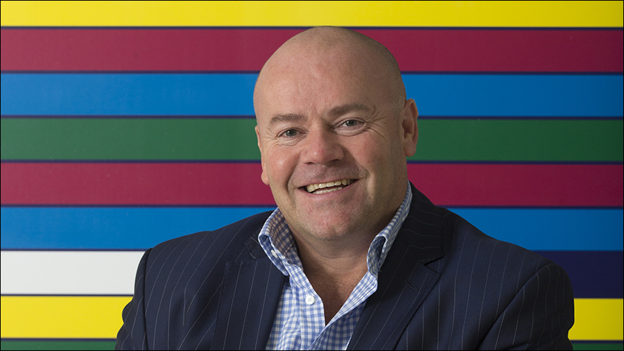 A man in a suit smiles in front of a colorful, striped background, embodying the perfect blend of professionalism and friendliness essential for effective people management.