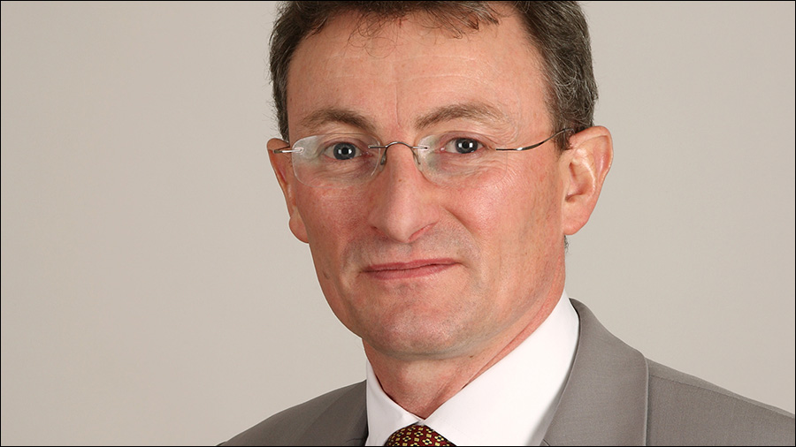 A man with glasses and a slight smile, likely part of the HR personnel, is wearing a gray suit and patterned tie as he stands against a plain background.