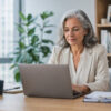 An older woman works at a laptop in an office.