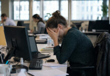 Government launches major overhaul of mental health care with focus on prevention A woman sits at an office desk with her head in her hands.