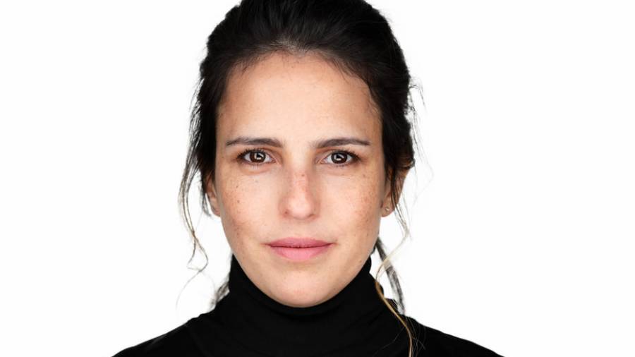 A person with dark hair is looking straight ahead, wearing a black turtleneck, against a white background, exuding the confidence of someone experienced in HR.