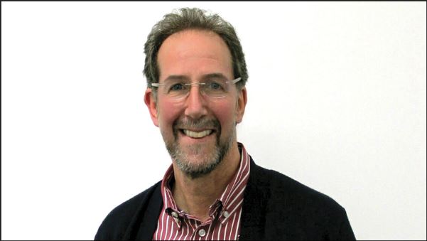 A man with glasses and a beard is smiling against a plain white background. He is wearing a black sweater over a red and white striped shirt, embodying the approachable demeanor often found in personnel management roles.