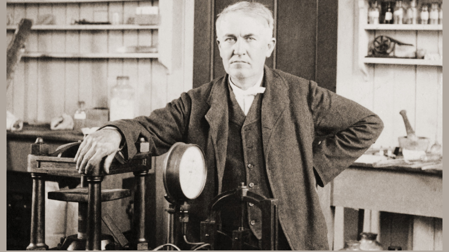 A man stands in a cluttered workshop, resting his hand on a machine in front of him, reflecting on preparations for his first job interview, with shelves and various equipment in the background.