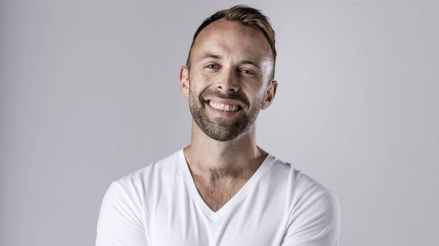 A man with short hair and a beard, likely an HR professional, smiles while wearing a white t-shirt against a plain background.