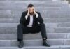 Money worries drive surge in workplace absence as four in five staff take time off A man in a suit sitting on steps with his head in hands.