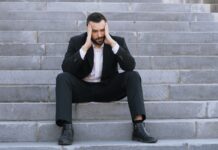 Money worries drive surge in workplace absence as four in five staff take time off A man in a suit sitting on steps with his head in hands.