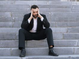 A man in a suit sitting on steps with his head in hands.