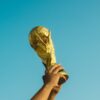 A person holding the World Cup trophy against the backdrop of a blue sky.