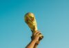 Employers urged to spot gambling harms during World Cup A person holding the World Cup trophy against the backdrop of a blue sky.