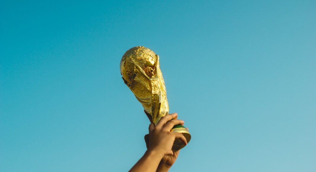 A person holding the World Cup trophy against the backdrop of a blue sky.