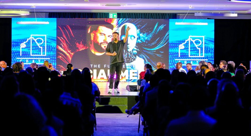 Photo by Carlos Gil A speaker presenting on stage to an audience.