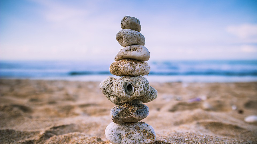 A stack of seven stones balanced on a sandy beach, with the sea and a blue sky in the background, reminiscent of harmony and balance in human resources.