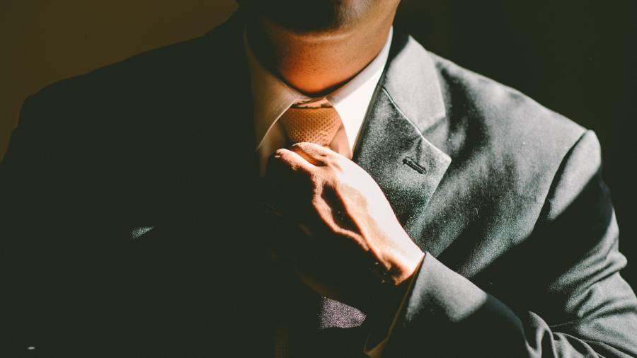 A person in a suit adjusts their yellow tie in a dimly lit setting, embodying the polished professionalism expected in Human Resources.