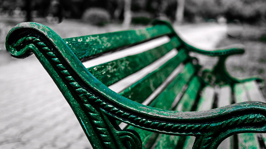 Close-up of a green metal park bench with intricate armrest designs. The background is blurred, showing a paved pathway and greenery, creating a serene spot for HR personnel to reflect on people management strategies.