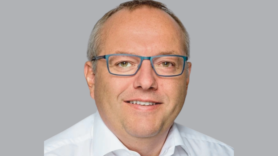 A middle-aged man with short gray hair and glasses wearing a white shirt, smiling against a plain gray background, radiating an air of expertise perhaps suited for discussions at COP26 or HR seminars.