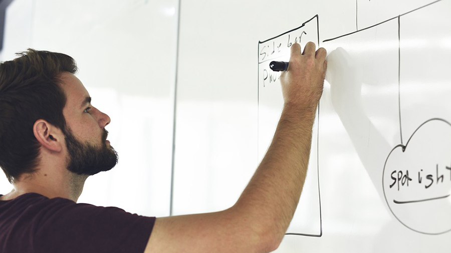 A man writes on a whiteboard, meticulously crafting a diagram with various labels for effective people management and HR strategies.