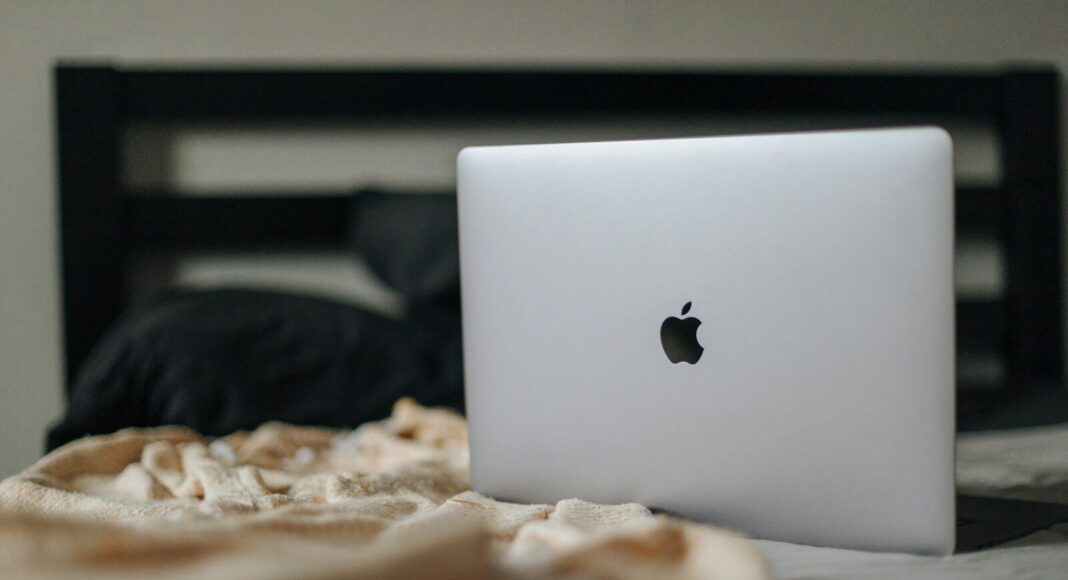 An apple laptop on a bed.