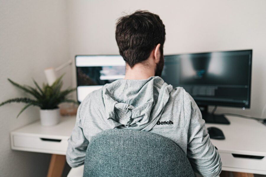 A young man in gray hoodie working on a laptop.