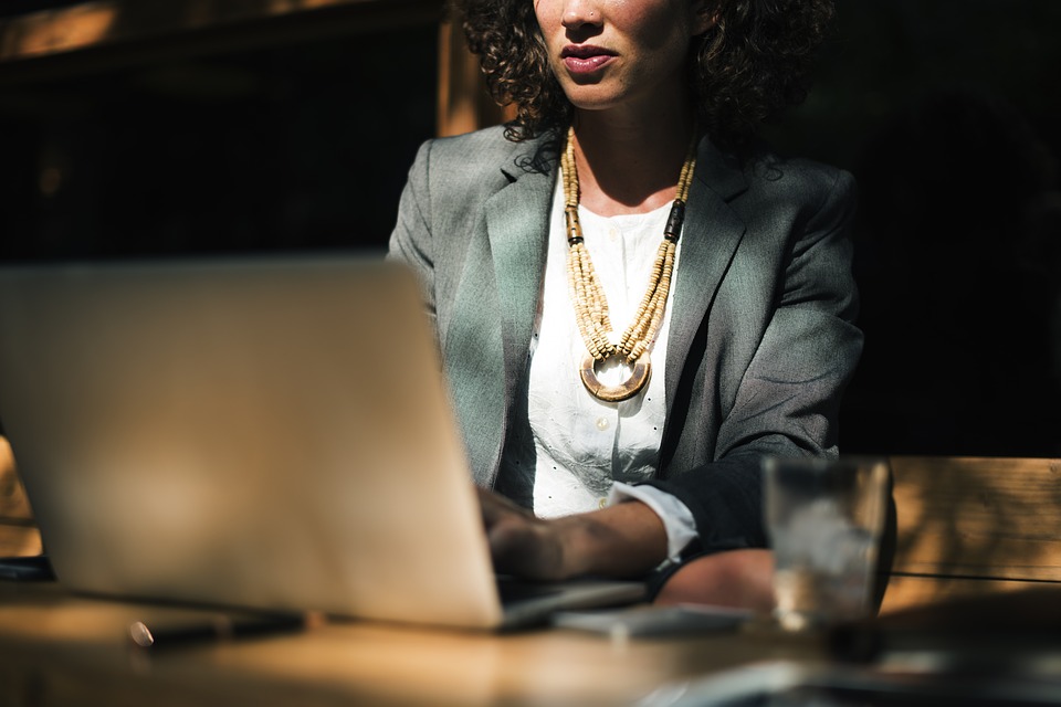 A person in a blazer and necklace sits at a table, working on a laptop, likely reviewing HR strategies or focusing on people management tasks.