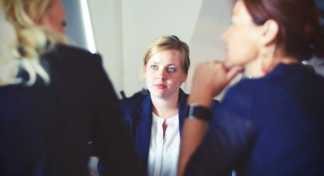 A woman sits across a table from two other women, as she is interviewed.
