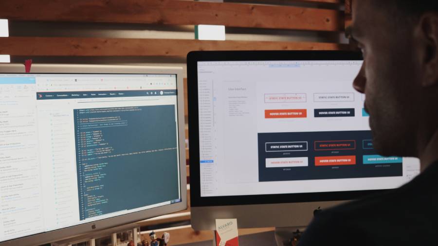 A person working at a desk with two monitors, one displaying computer code and the other showing a user interface design, is seamlessly integrating technical skills with human resources by optimizing personnel management software.