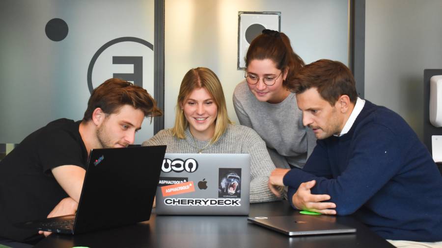 Four people are seated and gathered around two laptops, collaborating and smiling, perhaps brainstorming in a Human Resources meeting.