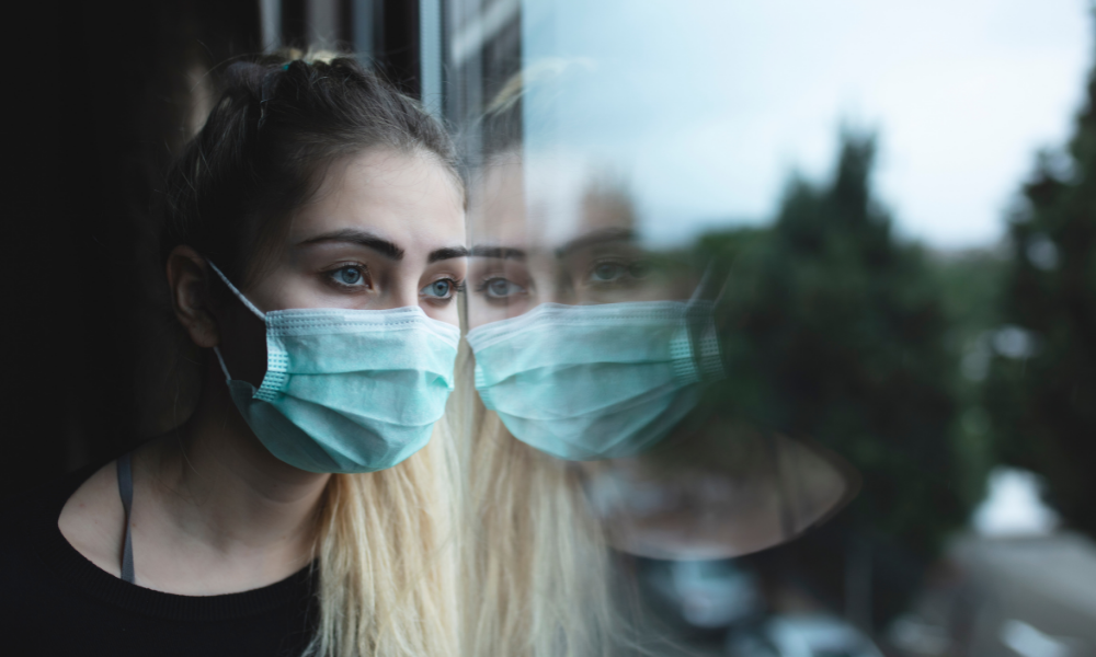 woman in mask looks out of window