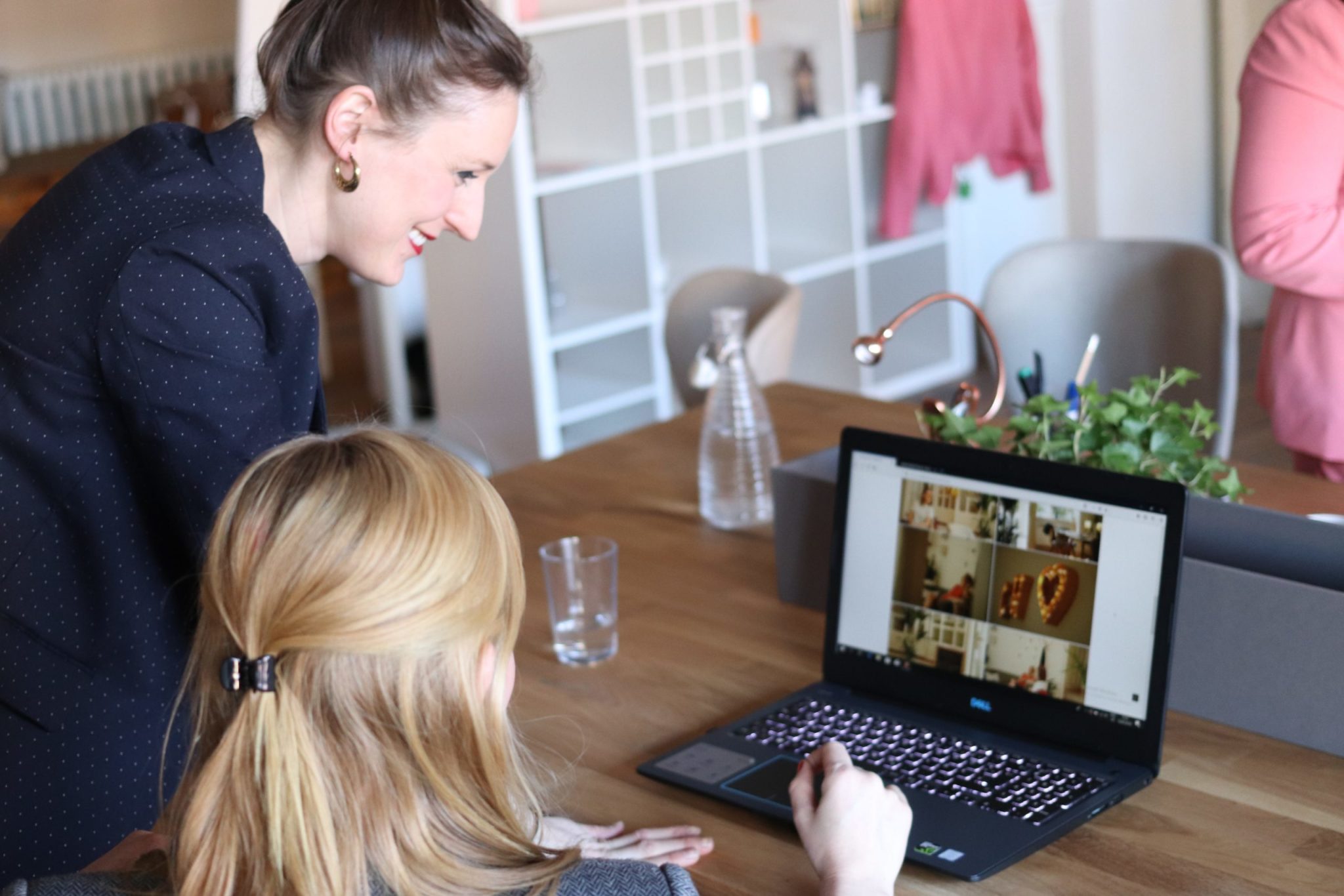 Two women are looking at a laptop screen together in an office setting; one woman is sitting and the other is standing, both appearing engaged with the content on the screen, likely discussing HR policies or personnel-related decisions.