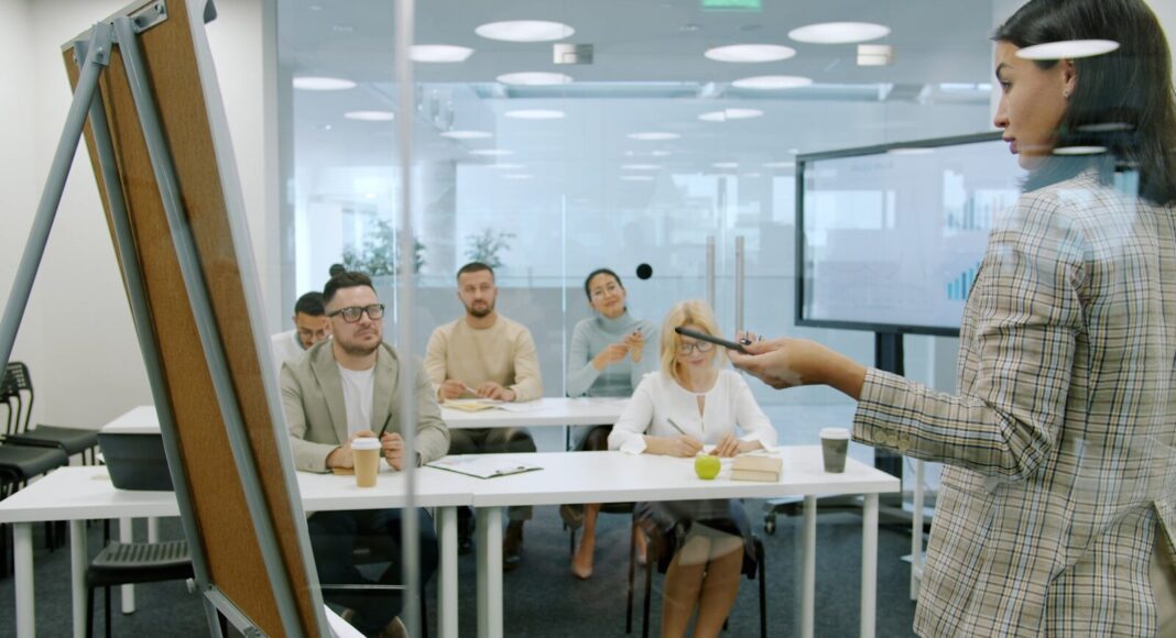 Photo by Vitaly Gariev Staff take part in a learning session, seated at desks while an instructor talks at a board in front.