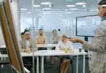 Lack of time leaves workplace learning ‘squeezed out’ Staff take part in a learning session, seated at desks while an instructor talks at a board in front.