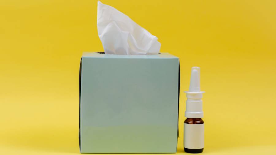 A box of tissues and a nasal spray bottle are placed against a yellow background, creating an essential kit for HR personnel to keep on hand.