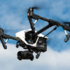 A quadcopter drone with a camera attached flies against a backdrop of a blue sky and clouds, capturing stunning aerial footage – perfect for showcasing your personnel in HR training videos.