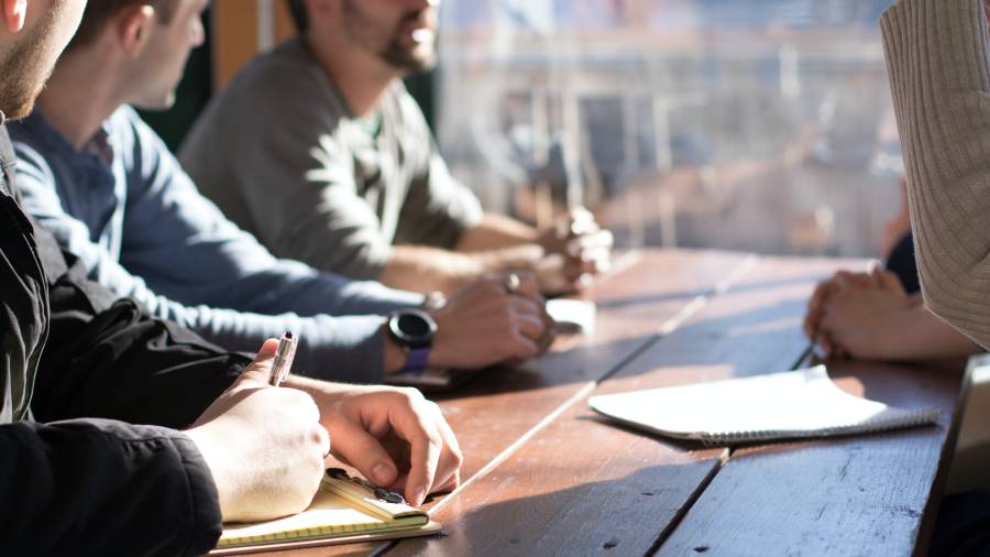 Personnel sitting at a table, engaged in discussion, with notebooks and pens on the table.