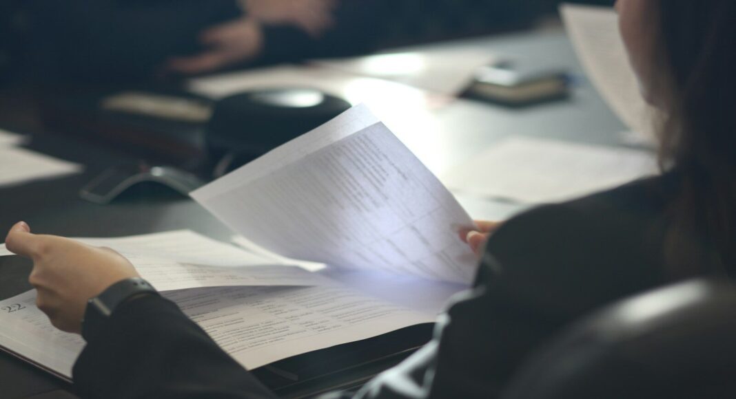 A person reads paper documents at a desk.