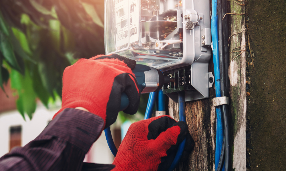 A person wearing red gloves uses a drill on a mounted electrical panel outdoors, following safety protocols stringently to avoid incidents like the one where a company was fined £1.5 million after a worker died due to negligence.