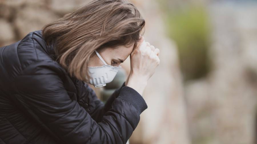 A woman wearing a mask and black jacket rests her forehead on her clasped hands, appearing deep in thought or contemplation, as if pondering over intricate issues related to human resources.