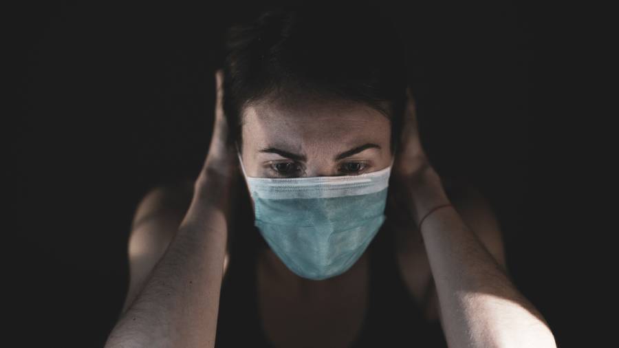 A person wearing a face mask holds their head, looking down with a serious expression in a dark setting, reflecting the heavy responsibilities of People Management.